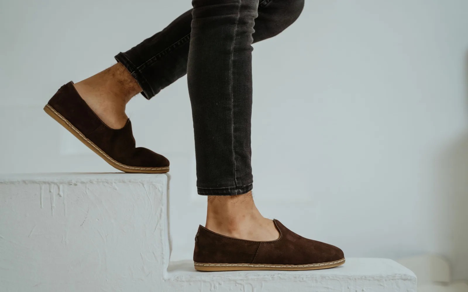 Jambes en jean noir et mocassins en daim marron sur une marche blanche