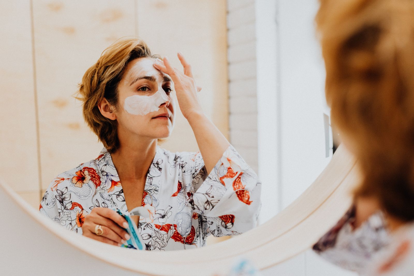 Femme qui applique un masque de soin devant un miroir rond